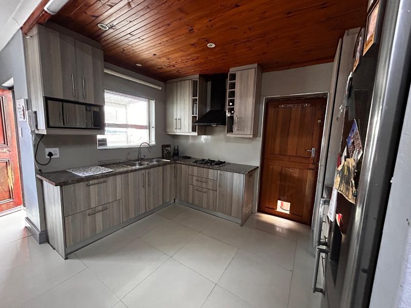 Modern kitchen featuring light wood-grain cabinetry, granite-look countertops, a gas hob with extractor, and a warm timber-paneled ceiling.