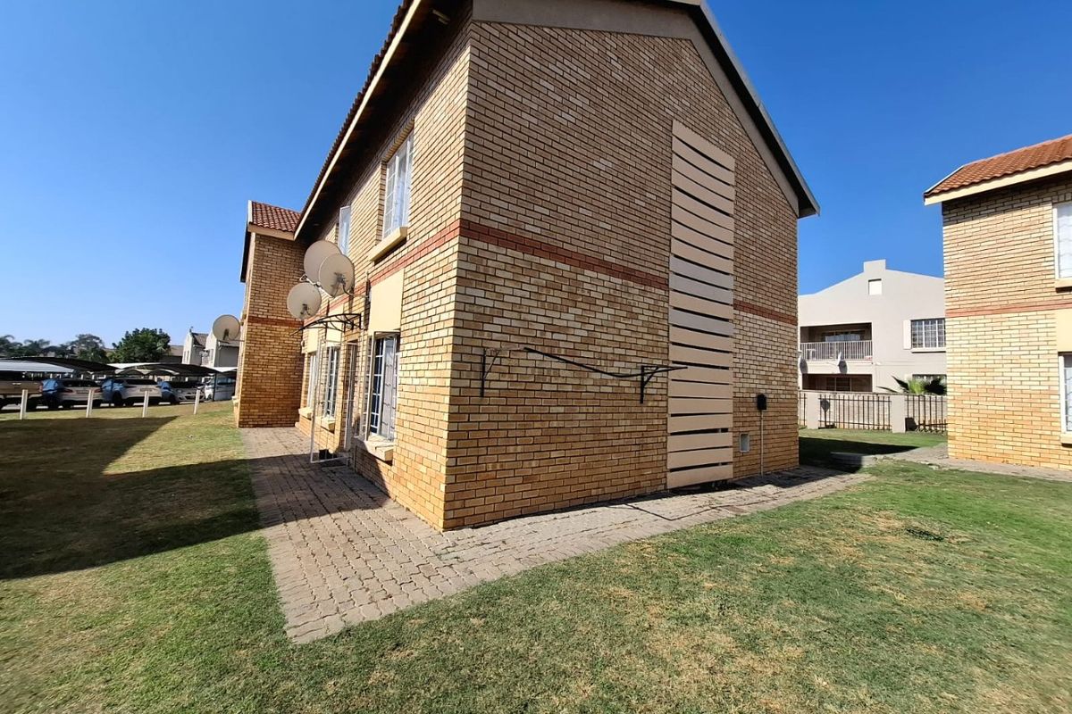 Exterior view of a face brick apartment building featuring a paved walkway, lawn area, and wall-mounted washing line.