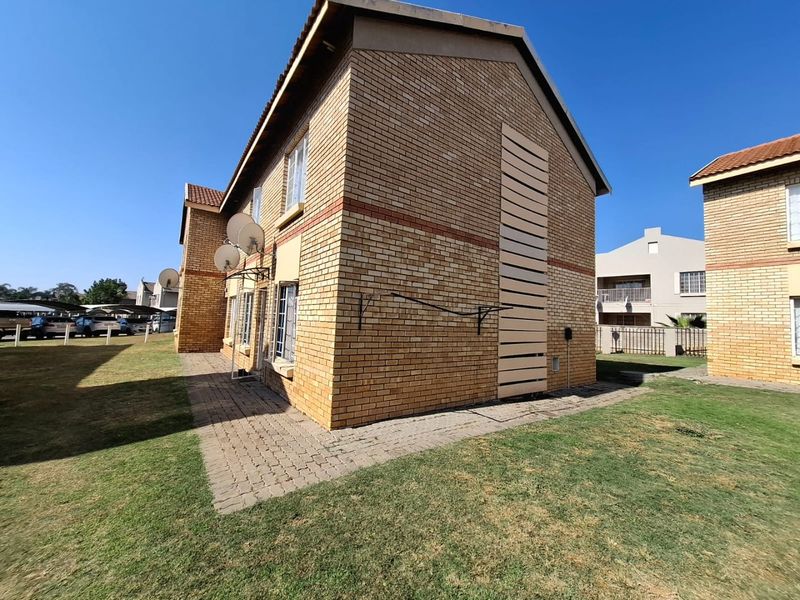 Exterior view of a face brick apartment building featuring a paved walkway, lawn area, and wall-mounted washing line.