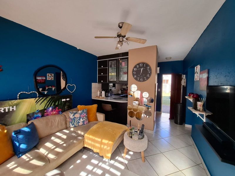 Open-plan living area featuring tiled flooring, a ceiling fan, and a compact kitchen nook with built-in cabinetry and counter space.