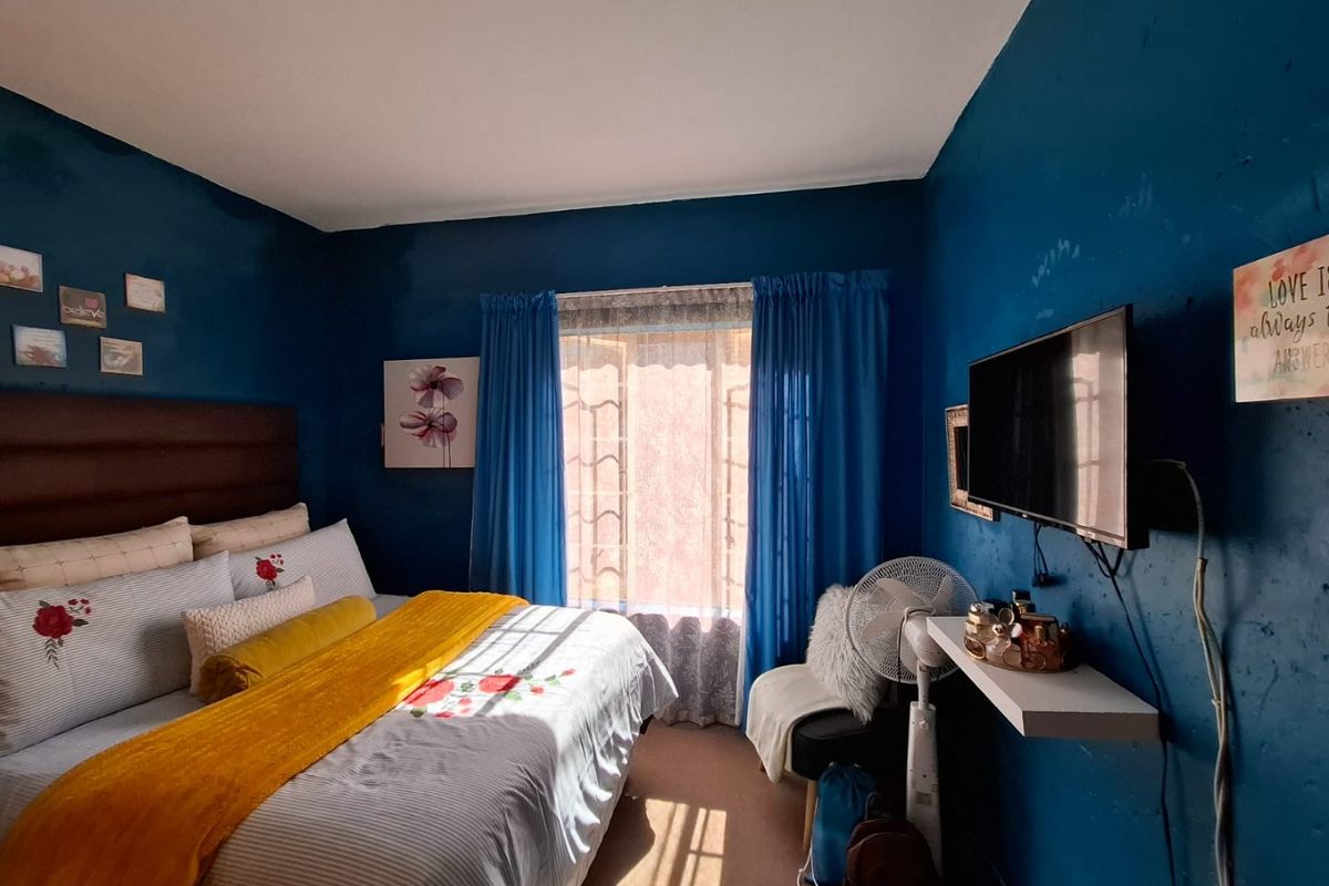 A bedroom featuring dark blue walls, a window with curtains, and a wall-mounted shelf. The room requires cosmetic updates to the wall finishes.