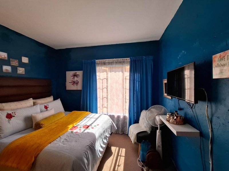 A bedroom featuring dark blue walls, a window with curtains, and a wall-mounted shelf. The room requires cosmetic updates to the wall finishes.