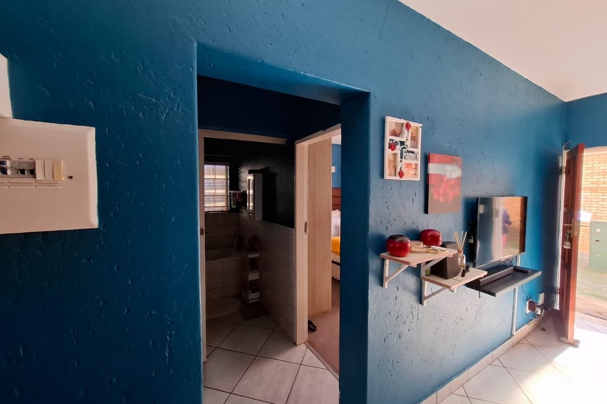 A living area featuring blue textured walls, tiled flooring, and an integrated electrical distribution board, with a doorway leading to an adjacent room.