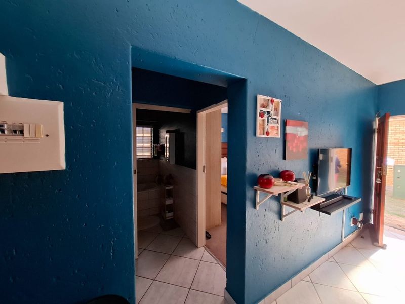 A living area featuring blue textured walls, tiled flooring, and an integrated electrical distribution board, with a doorway leading to an adjacent room.