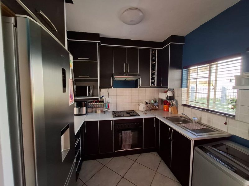 A functional kitchen featuring dark cabinetry, a built-in oven and hob, tiled backsplash, and a stainless steel sink with natural light from the window.