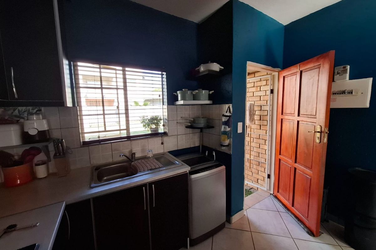 Compact kitchen featuring dark cabinetry, stainless steel sink, tiled backsplash, and direct access to an exterior area through a timber door.