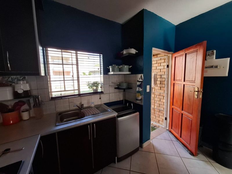 Compact kitchen featuring dark cabinetry, stainless steel sink, tiled backsplash, and direct access to an exterior area through a timber door.