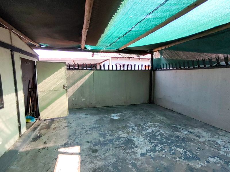 An outdoor patio area featuring concrete flooring, perimeter walls with security spikes, and a shade netting structure.