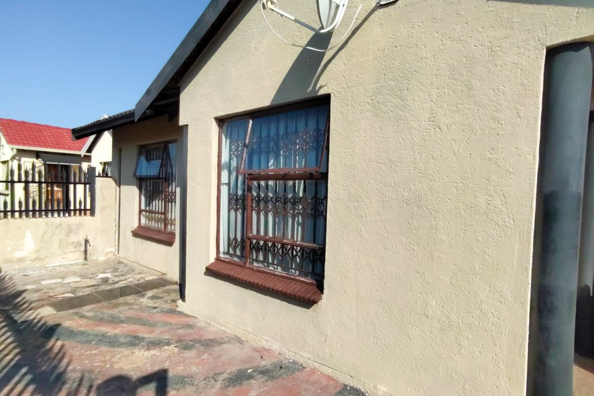 Rear exterior view of the property featuring plastered walls, security gates on windows, and a paved patio area.