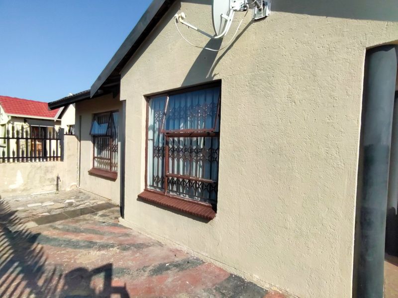 Rear exterior view of the property featuring plastered walls, security gates on windows, and a paved patio area.
