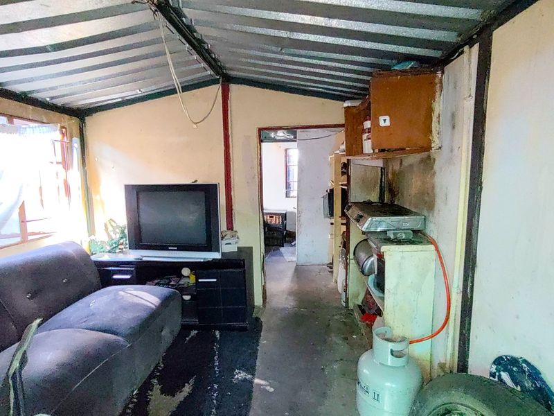 An open-plan living and kitchen area featuring a corrugated metal ceiling and basic built-in kitchen shelving, requiring significant renovation and cosmetic updates.