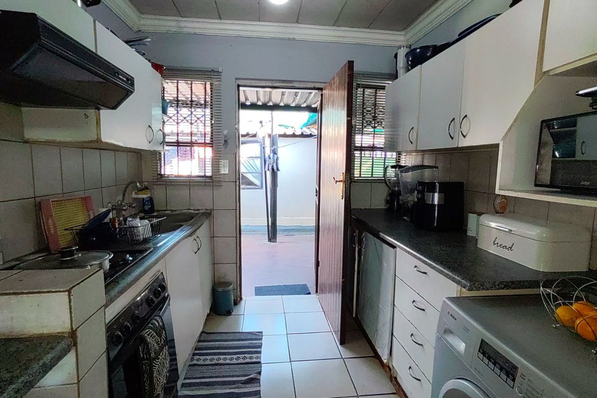 A functional galley-style kitchen featuring built-in cabinetry, tiled backsplash, and direct access to an outdoor area, offering potential for modern renovation.