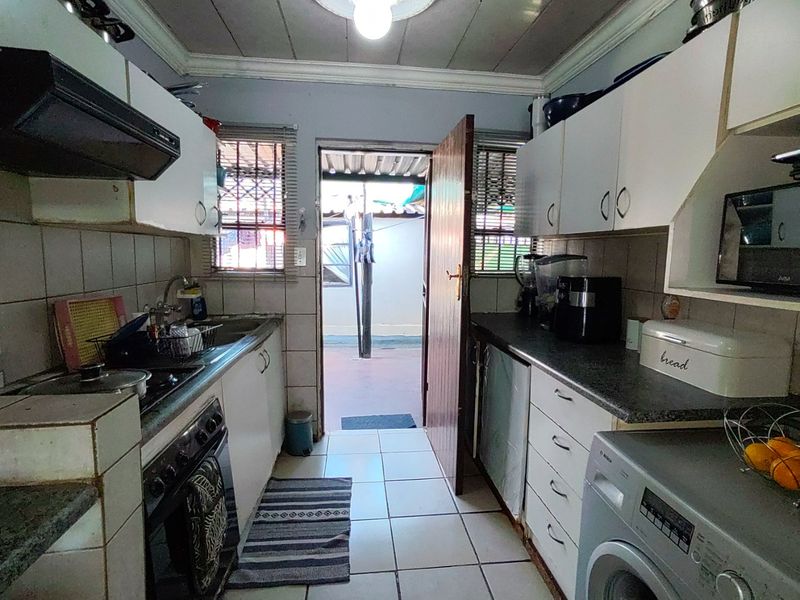 A functional galley-style kitchen featuring built-in cabinetry, tiled backsplash, and direct access to an outdoor area, offering potential for modern renovation.