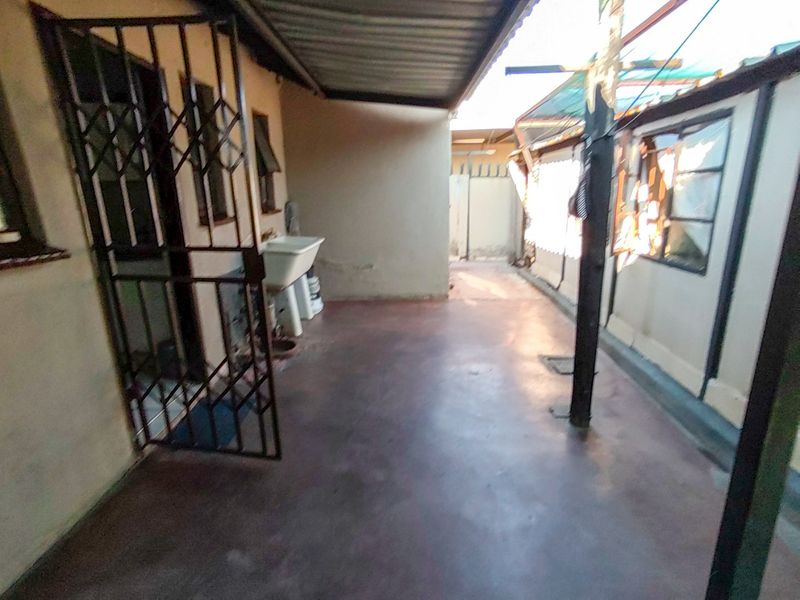 A covered outdoor utility area featuring a concrete floor, security gate, and a fixed utility sink, suitable for laundry or storage purposes.