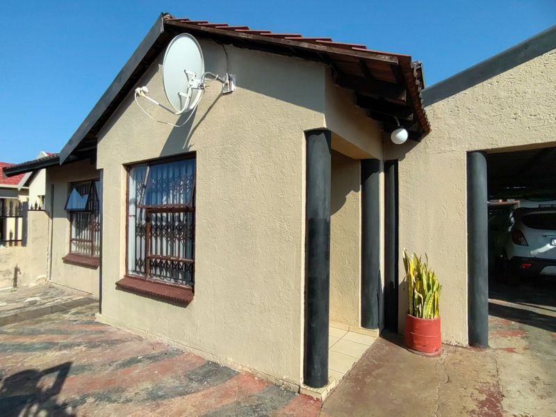 Front exterior view of the house featuring a tiled roof, concrete columns, and a paved driveway with security bars on the windows.