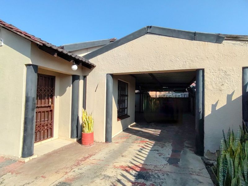 Front exterior view of the property featuring a covered carport, security gates, and a concrete driveway with visible wear.
