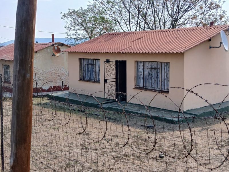 A detached single-story house featuring a corrugated metal roof, security gates, and burglar bars, enclosed by a wire fence with razor wire.