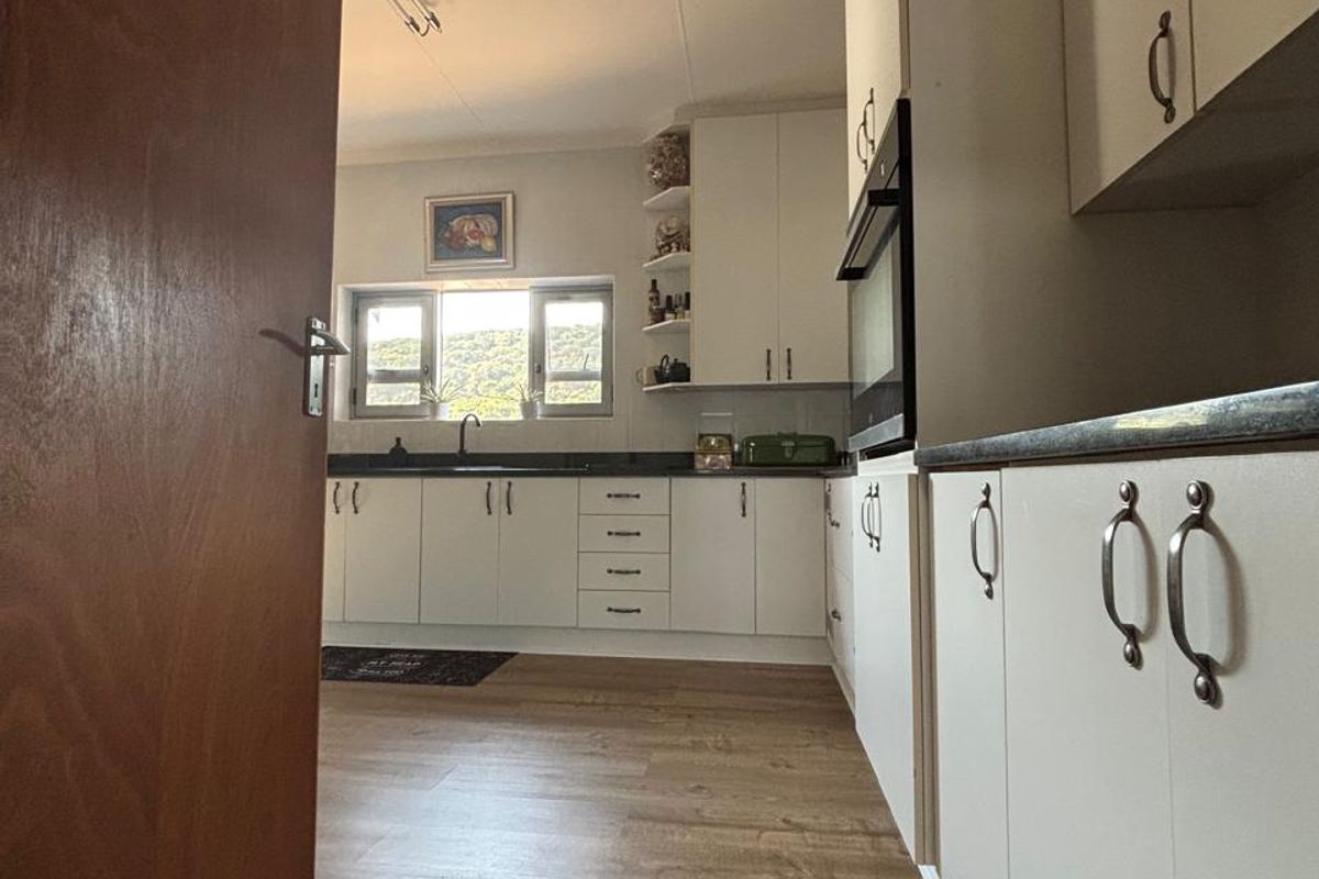 A functional kitchen featuring white cabinetry, dark stone countertops, integrated oven, and wood-look laminate flooring with natural light.