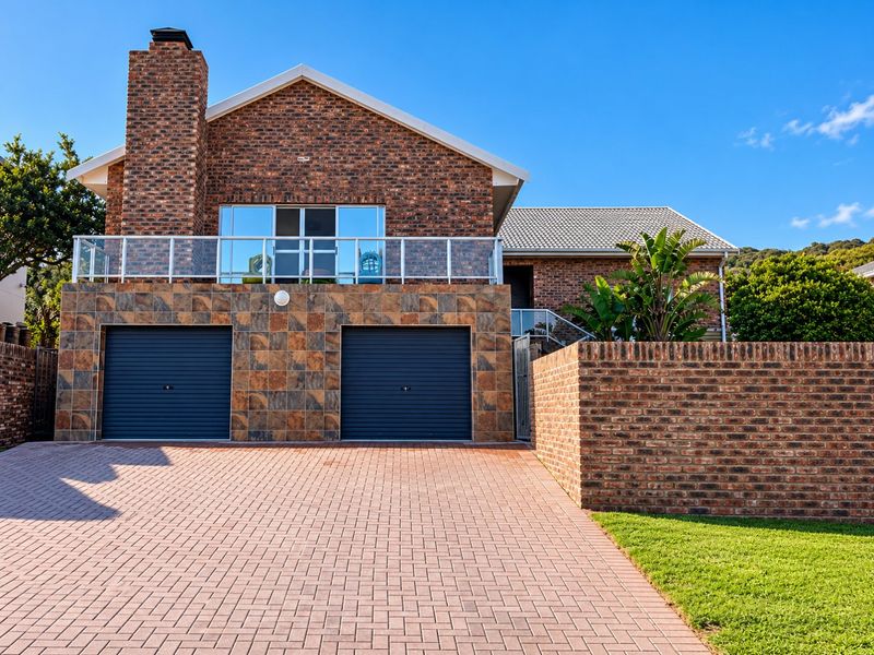 A well-maintained double-story brick home featuring a double garage, paved driveway, and an upper-level balcony with a modern glass balustrade.