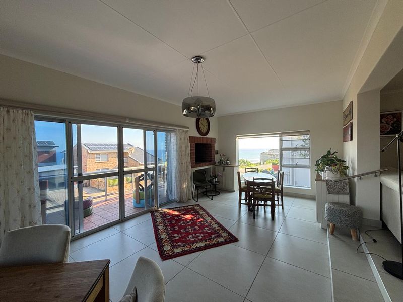 Spacious open-plan living area featuring large windows, sliding doors to a balcony, and a built-in brick fireplace with ocean views.