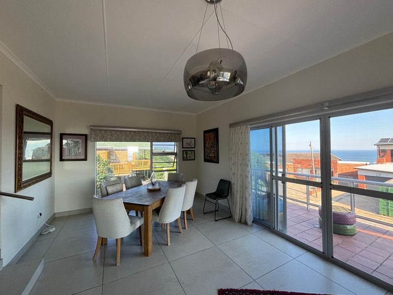 Bright dining area featuring large windows, tiled flooring, and sliding glass doors that open onto an outdoor balcony with coastal views.