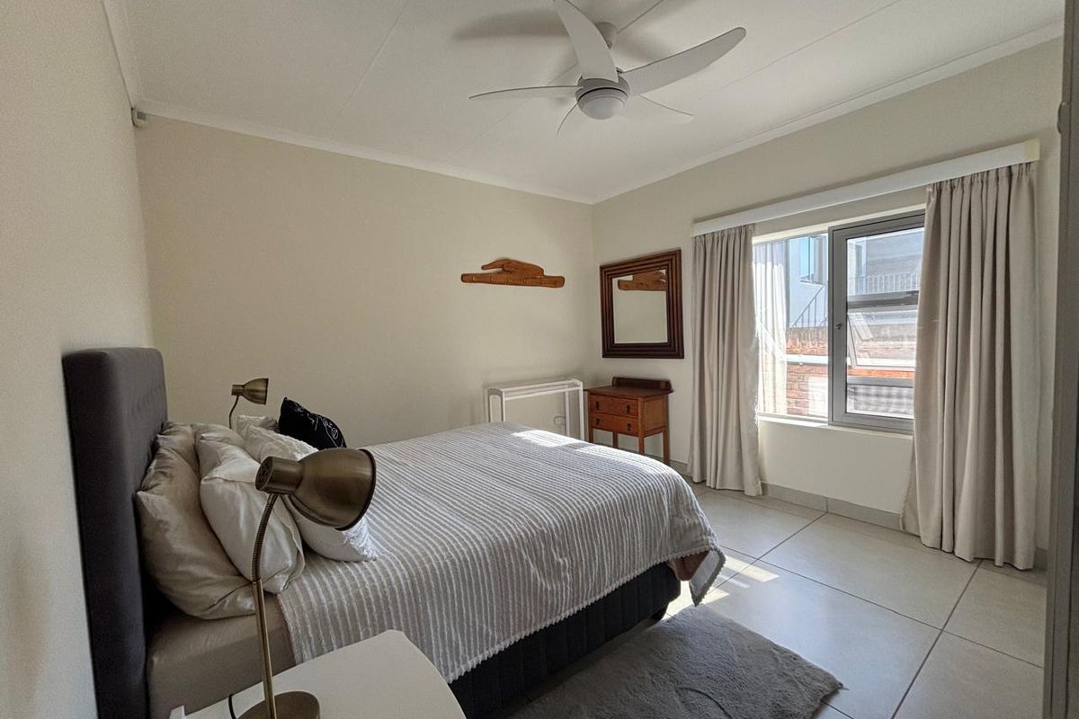 A well-maintained bedroom featuring neutral tiled flooring, a ceiling fan, and large windows that provide natural light.