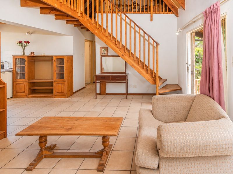Open plan living area featuring tiled flooring, a prominent wooden staircase, and direct access to the outdoor space through a sliding glass door.