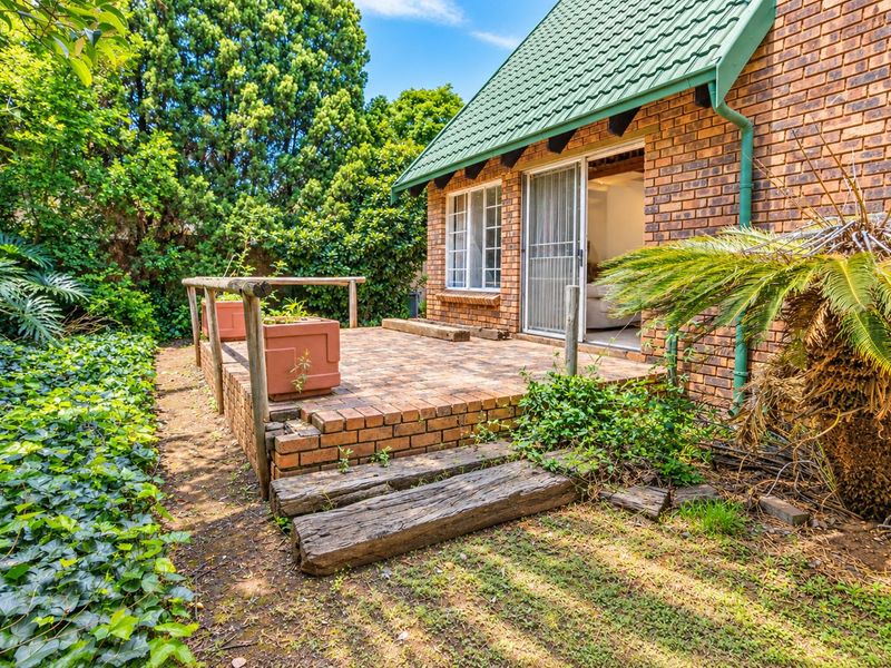 A private brick-paved patio area featuring timber railings and direct access to the interior through a sliding glass door, set within a garden.