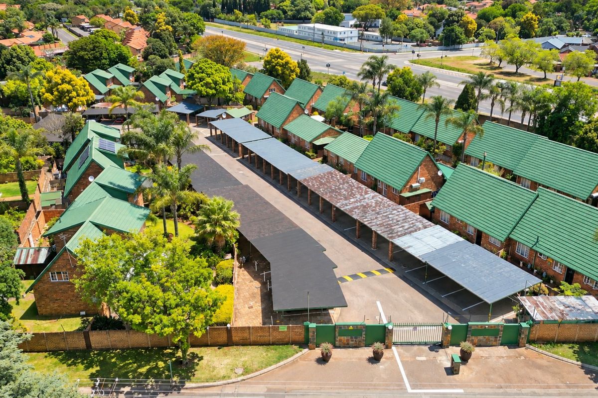Aerial view of a townhouse complex featuring multiple units with green tiled roofs, covered carports, and secure gated access.