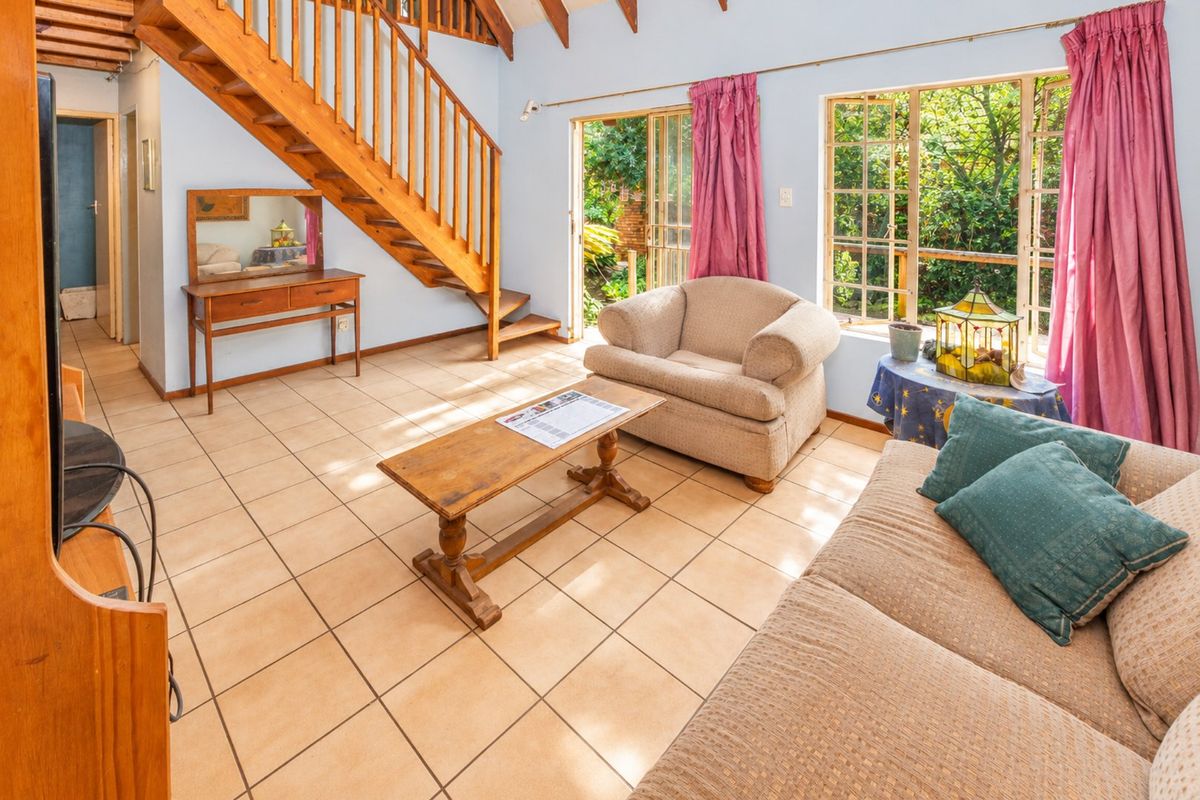 Spacious living room featuring tiled flooring, exposed timber rafters, and a wooden staircase, with direct access to the garden through sliding glass doors.