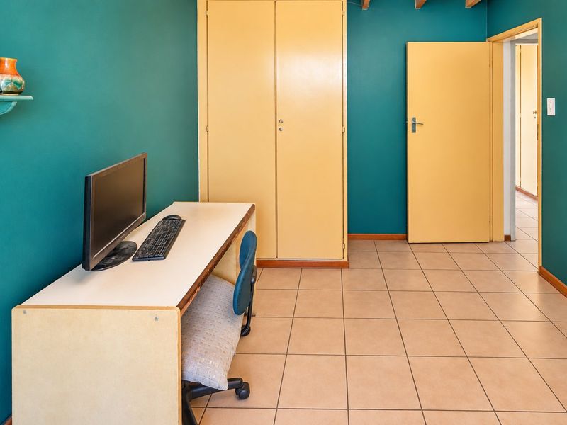 A bedroom featuring tiled flooring, built-in cupboards, and bold teal wall paint, offering a functional space with potential for modern updates.