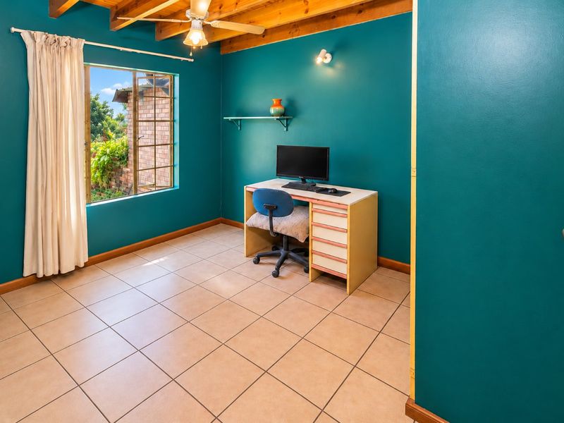A bedroom featuring exposed timber ceiling beams, a ceiling fan, and ceramic floor tiles, finished with bold teal wall paint.