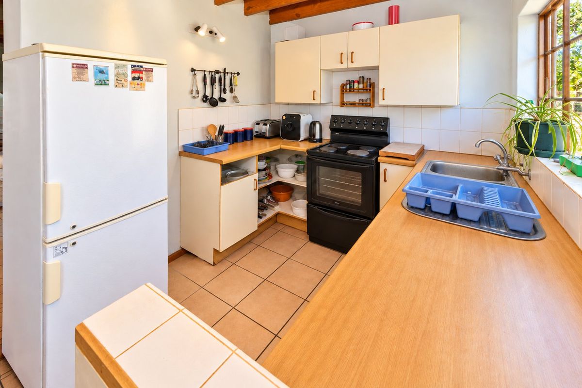 A functional kitchen featuring laminate countertops, tiled flooring, built-in cabinetry, a stainless steel sink, and exposed timber ceiling beams.