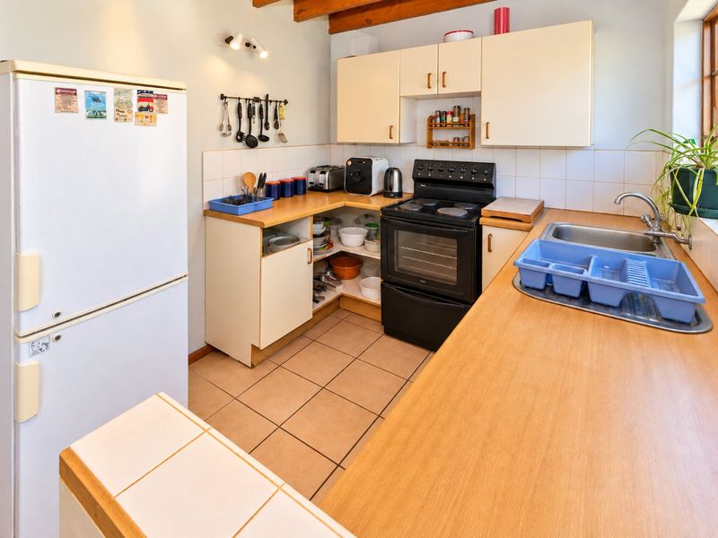 A functional kitchen featuring laminate countertops, tiled flooring, built-in cabinetry, a stainless steel sink, and exposed timber ceiling beams.