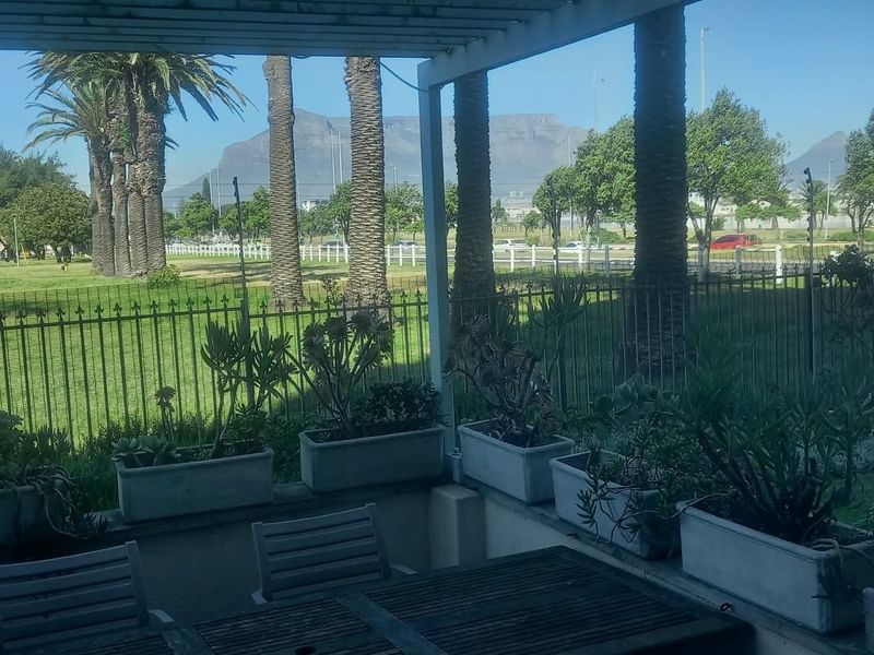 A covered patio area featuring a pergola structure, built-in concrete planters, and metal fencing, offering scenic views of the surrounding landscape and mountains.