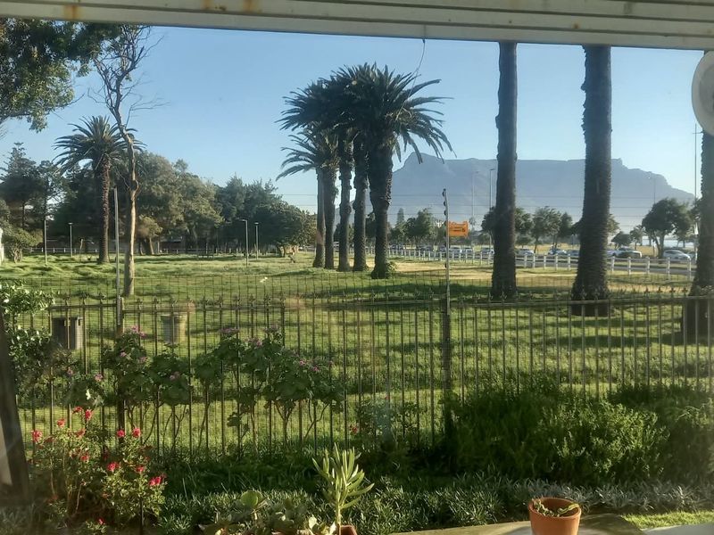 A scenic view overlooking a landscaped garden and metal fencing, with a prominent mountain range visible in the background.