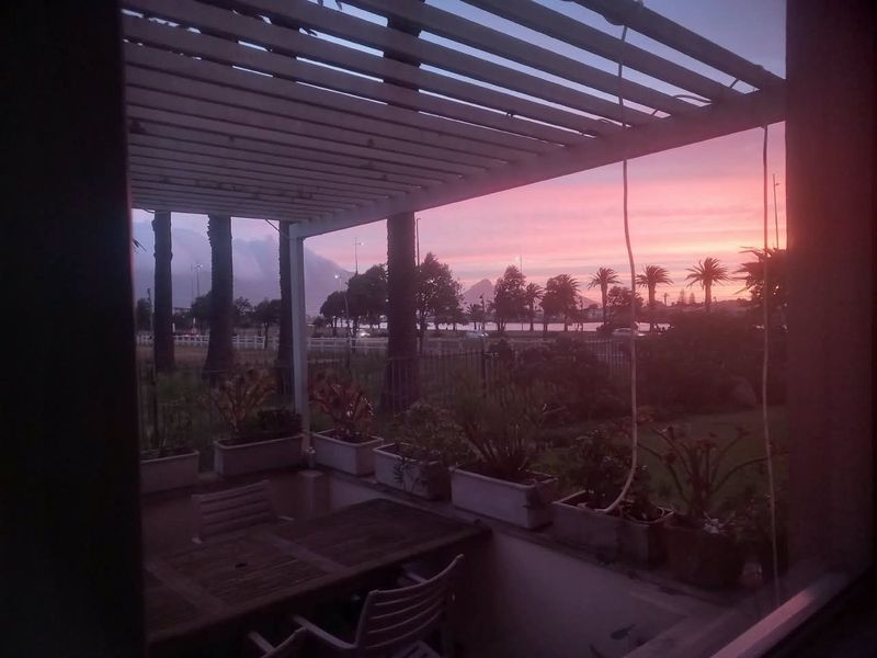 A covered patio area featuring a pergola structure, overlooking a garden with scenic sunset views.