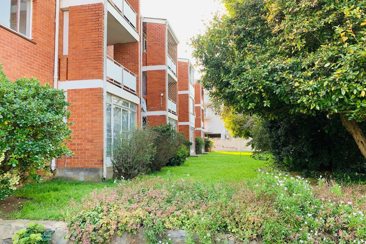 A view of the rear facade of a face brick apartment building featuring private balconies and a well-maintained communal garden area.