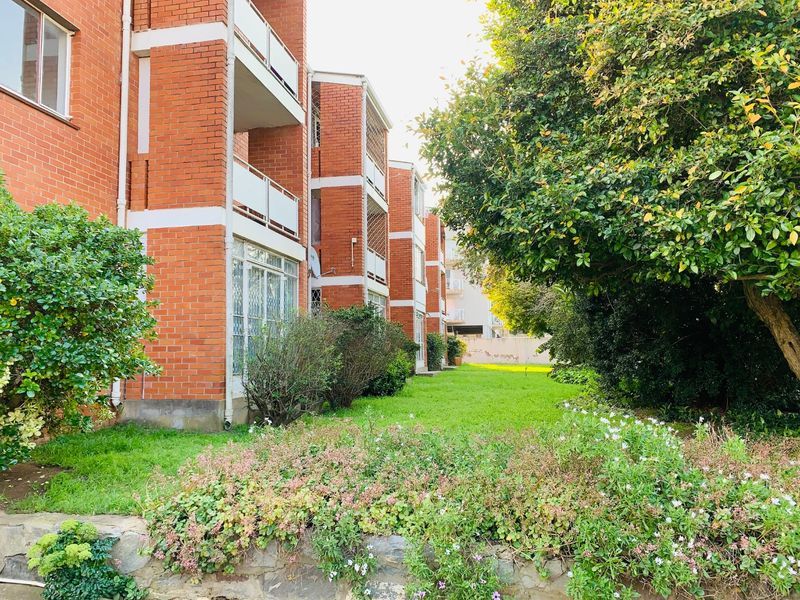 A view of the rear facade of a face brick apartment building featuring private balconies and a well-maintained communal garden area.