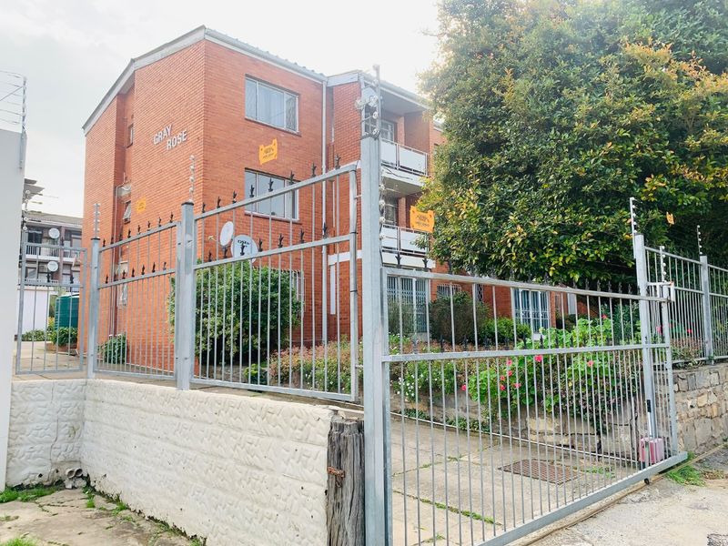 Front exterior view of the Gray Rose apartment complex featuring face brick construction, secure metal fencing, and established garden landscaping.