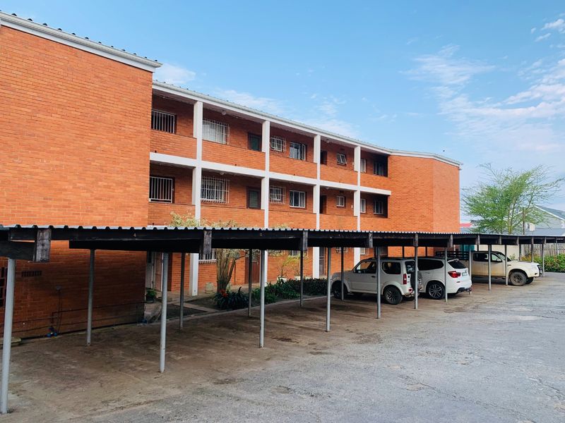 Exterior view of a multi-story brick apartment building featuring a covered parking area and security bars on windows.