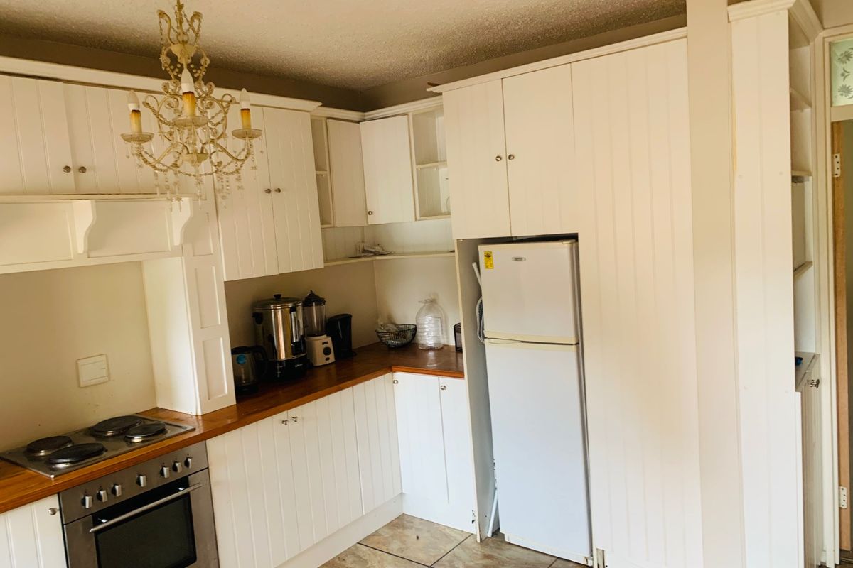 A functional kitchen featuring white built-in cabinetry, wooden countertops, and integrated oven and hob, with tiled flooring throughout.