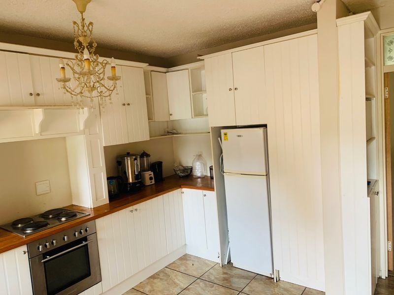 A functional kitchen featuring white built-in cabinetry, wooden countertops, and integrated oven and hob, with tiled flooring throughout.
