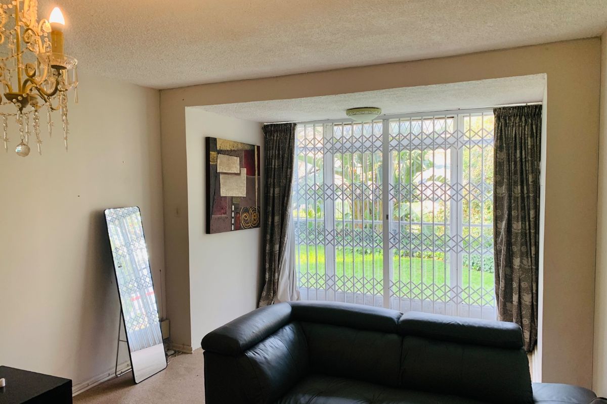 A living room featuring a sliding glass door with a security gate, providing access to the garden area.