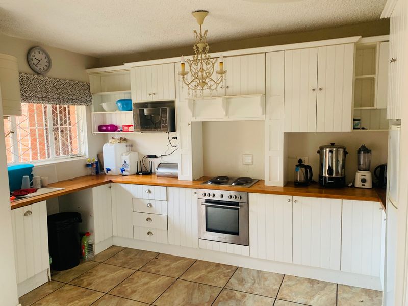 A functional kitchen featuring white cabinetry, wooden countertops, built-in oven and hob, and tiled flooring with security bars on the window.