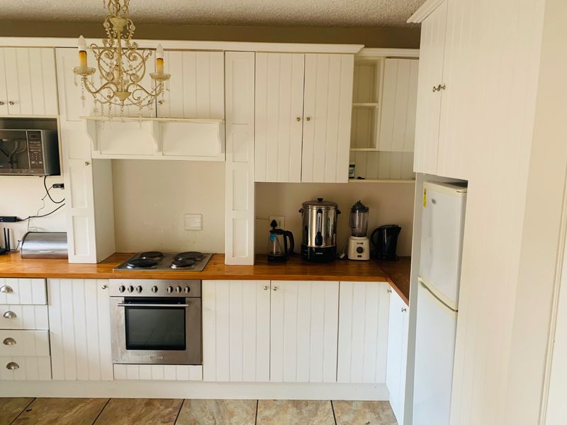 A functional kitchen featuring white cabinetry, wooden countertops, built-in oven and hob, and tiled flooring, offering a classic aesthetic with potential for modern updates.