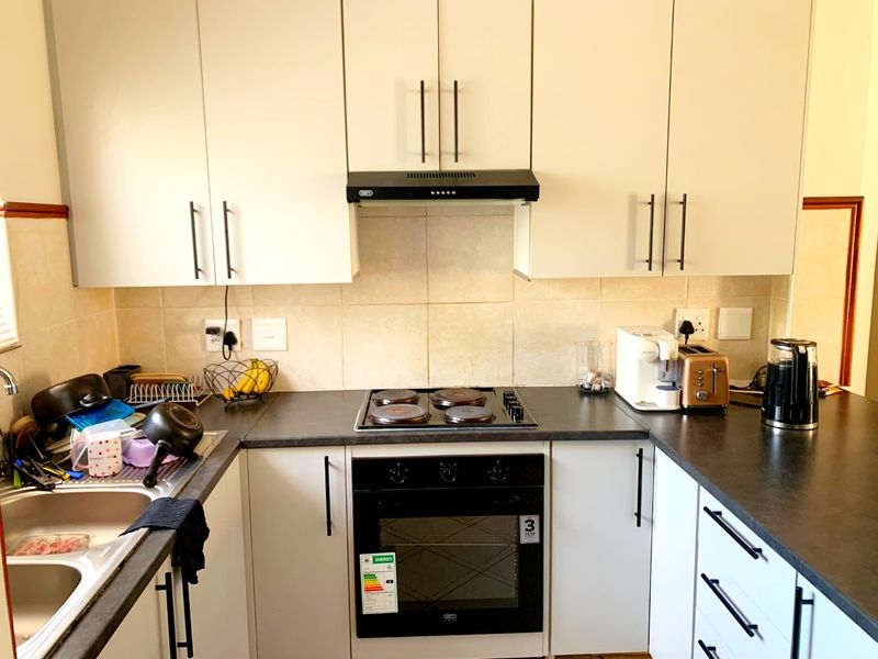 A functional kitchen featuring white cabinetry, dark laminate countertops, a built-in oven with electric hob, extractor fan, and a double bowl stainless steel sink.