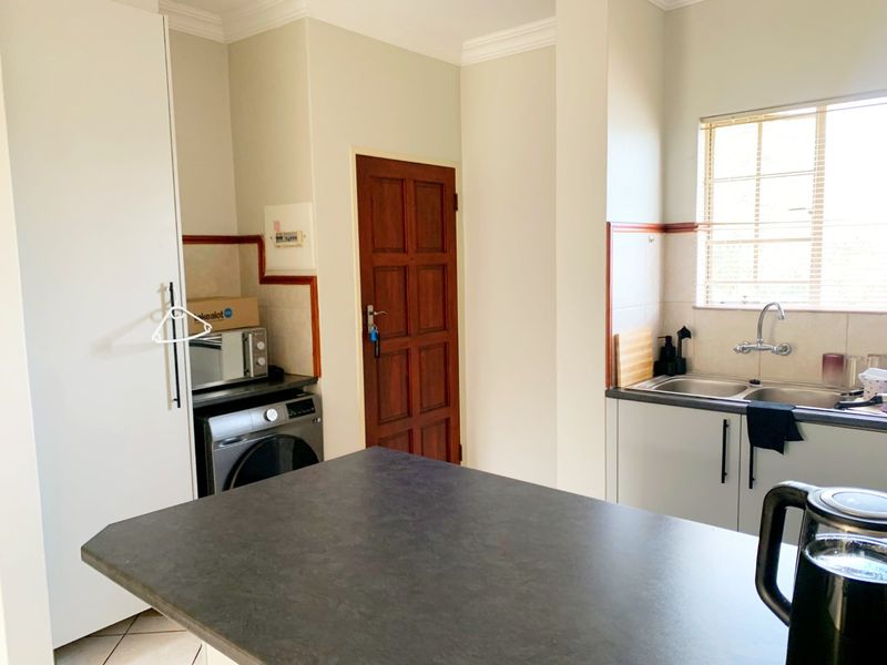A functional kitchen featuring built-in cabinetry, a double basin sink, laminate countertops, and a tiled backsplash with natural light from the window.