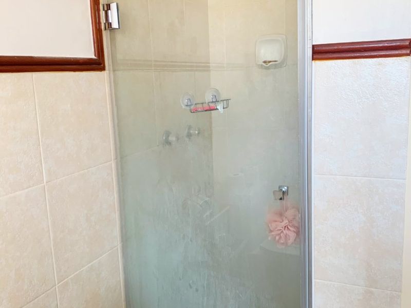 A functional bathroom shower enclosure featuring tiled walls and a glass door, requiring some maintenance to restore its finish.