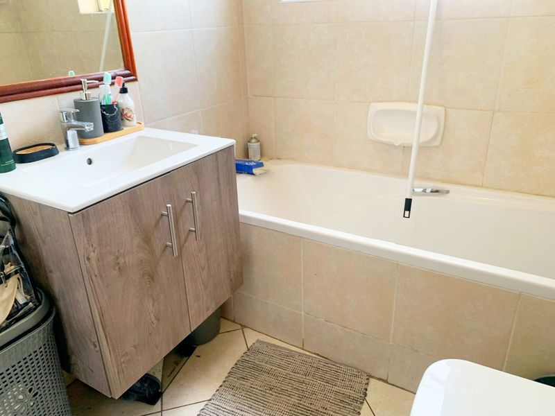 A functional bathroom featuring a wood-finish vanity cabinet, ceramic basin, and a built-in bathtub with neutral wall tiling.